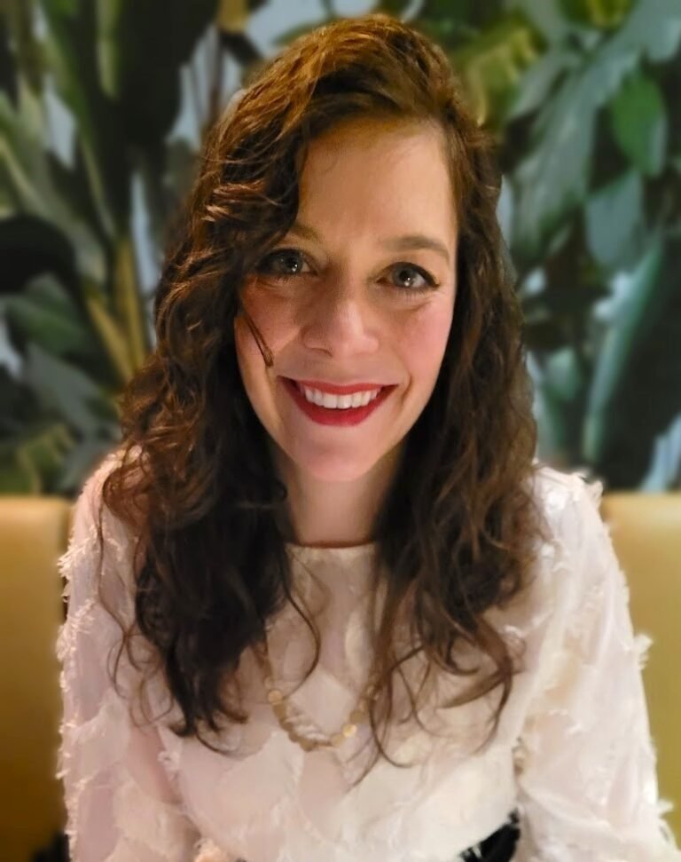 A portrait of Alexandra Emonts, founder of Edoaria, smiling in a green lush room.
