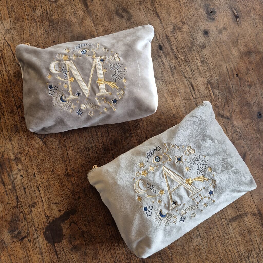 Two Edoaria Ciel des Rêves Grand Toiletry Bags elegantly placed on an old castle wood table, showcasing celestial embroidery in blue, gold, and cream.