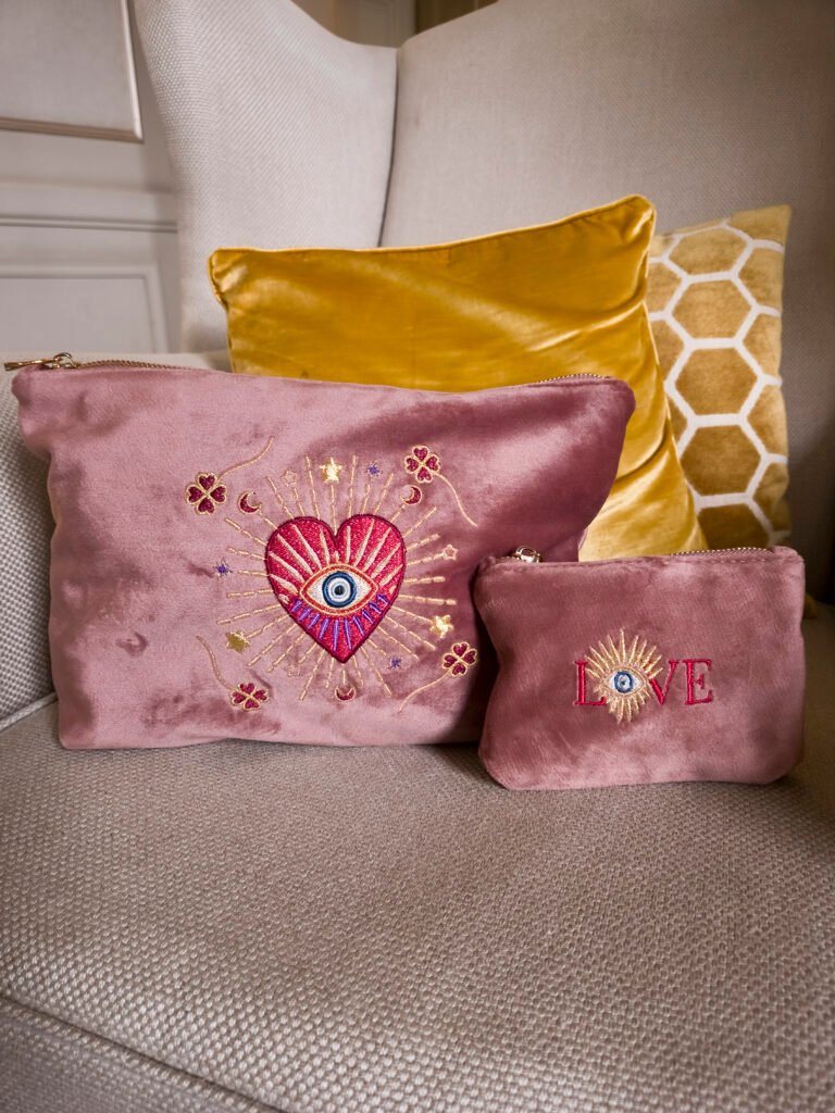 Edoaria Rouge Amour Grand Toiletry Bag and Essentials Sleek Pouch elegantly placed on a beige chair with gold cushions, creating a luxurious and romantic setting.