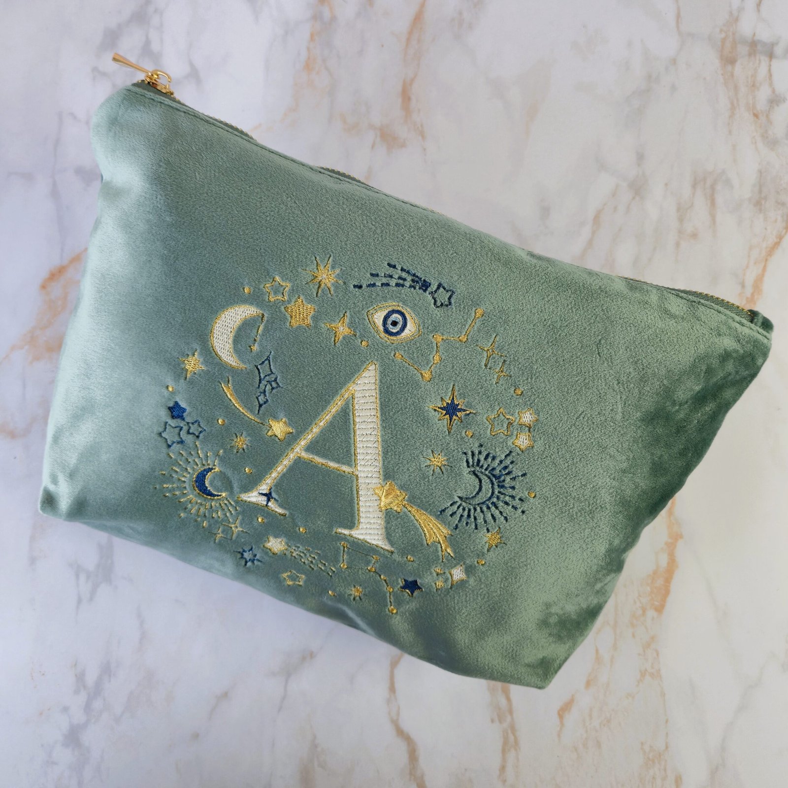 Flat lay of the Aqua Marine velvet pouch with celestial gold and blue embroidery and the letter "A," Ciel des Rêves collection by Edoaria.