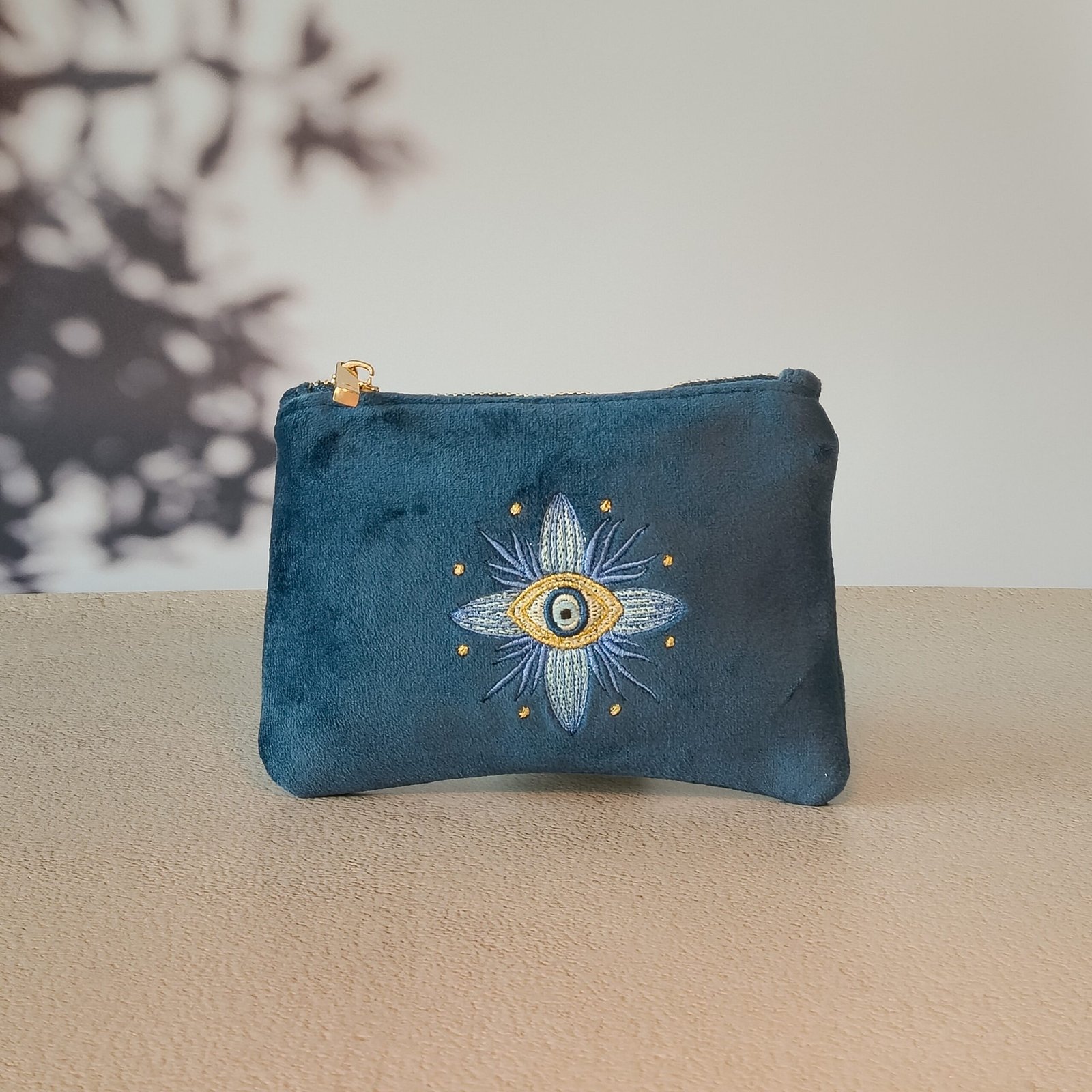 A sapphire blue velvet Essentials Sleek Pouch featuring an Art Nouveau floral design with a Greek Mati at the center.