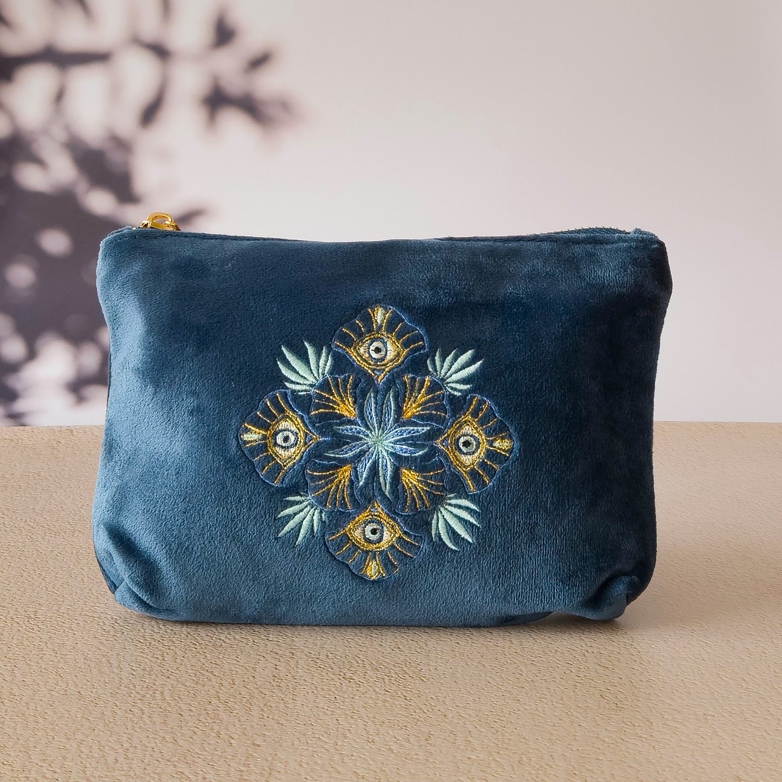 Jardin des Cyclades Petite trousse de maquillage - Broderie Arabesque et Oeil maléfique A Petite Makeup Bag in deep sapphire blue velvet with intricate Arabesque and Greek Mati embroidery, set against an ancient Greek temple floor.