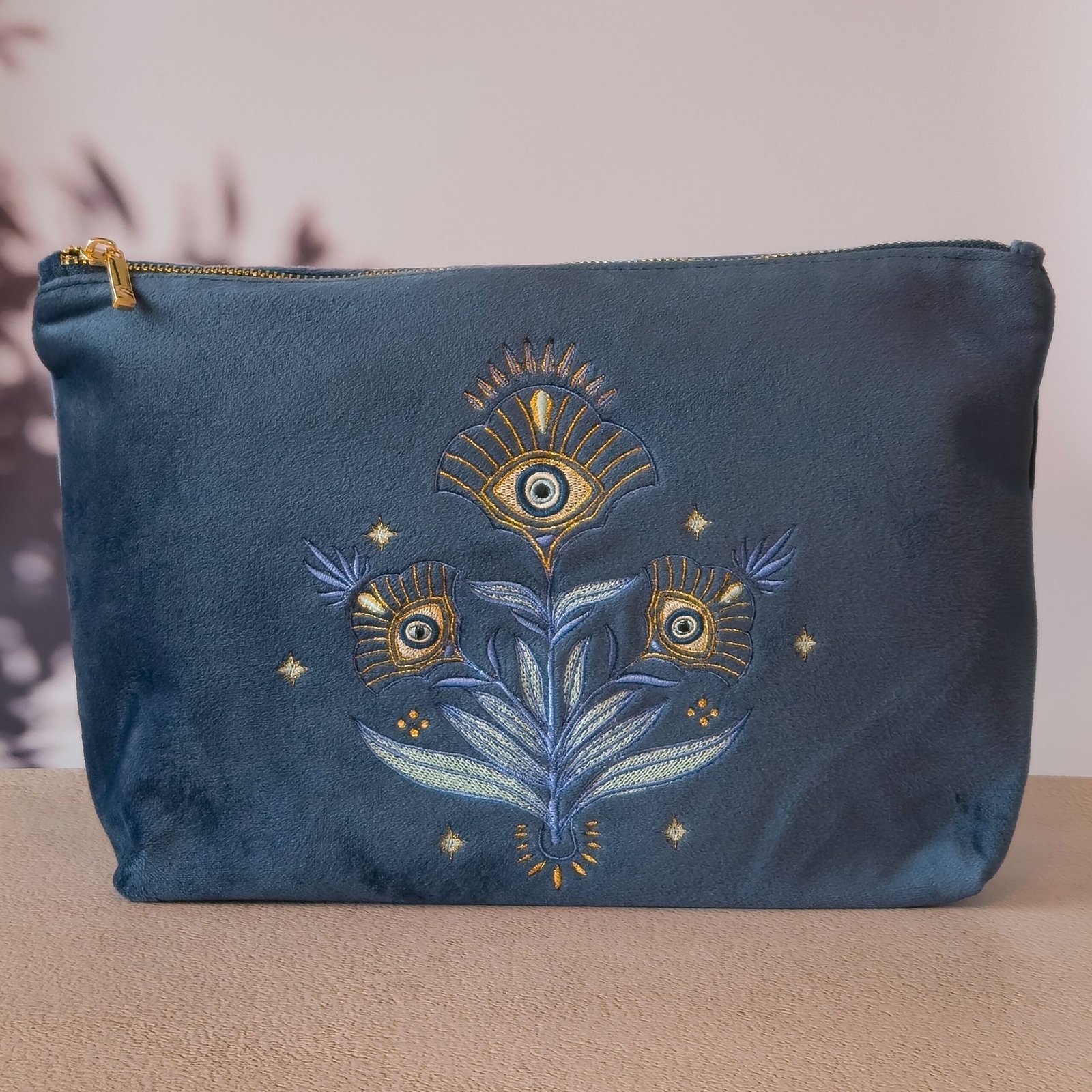 A luxurious deep sapphire blue velvet Grand Toiletry Bag featuring an Art Nouveau floral design intertwined with a protective Greek evil eye motif, set against an ancient Greek temple floor.