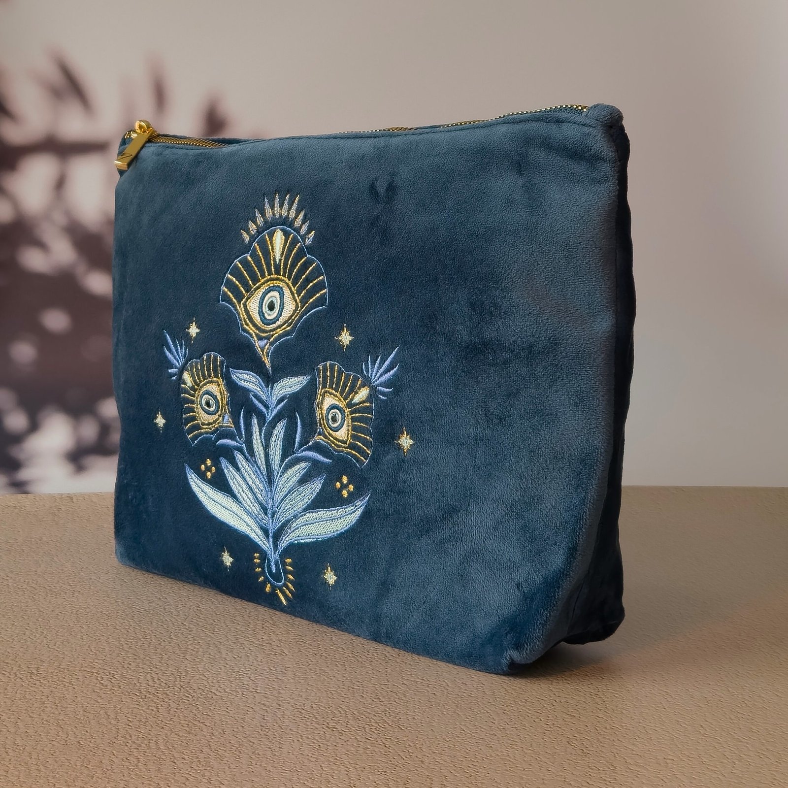 Close-up of the Grand Toiletry Bag’s intricate Art Nouveau floral embroidery with the Greek evil eye symbol, on deep sapphire blue velvet.