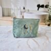 Ciel des Rêves Petite trousse de maquillage - Vue de face en Aqua MarineVelvet Front view of the Ciel des Rêves Petite Makeup Bag in Aqua Marine teal velvet, featuring moon, stars, and evil eye embroidery in blue, gold, and cream.