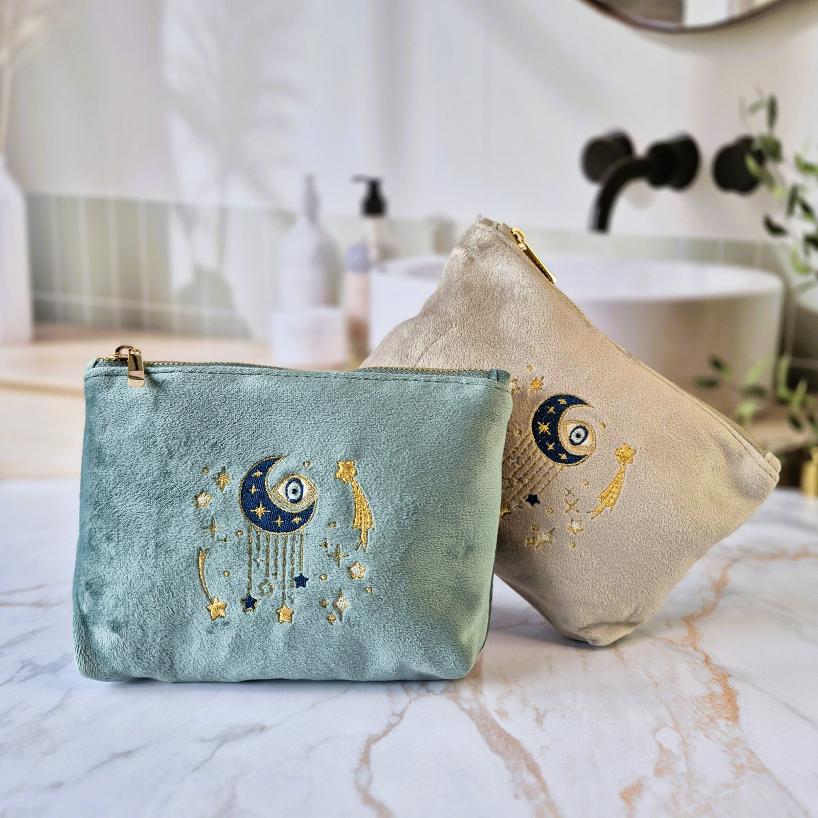 Pochette en velours Ciel des Rêves - Teal Aqua Marine et Beige Moonstone avec broderie or et bleu Edoaria Ciel des Rêves Petite Makeup Bags elegantly placed on a mable top counter bathroom, creating a luxurious and pampering setting.