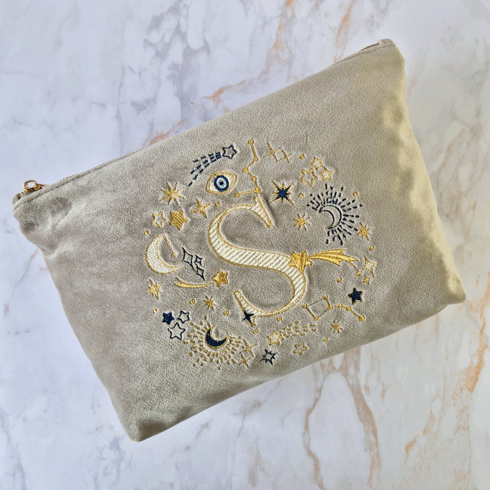 Flat Lay: Ciel des Rêves Velvet Pouch with Letter "S" Flat lay of the Beige Moonstone velvet pouch with celestial gold and blue embroidery and the letter "S," Ciel des Rêves collection by Edoaria.