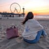 Alexandra, our owner, wearing the Edoaria our mixed cotton embroidered sweatshirt with zipped polo neckline from the Jardin des cyclades collection. Looking at a sunset on a Ferris Wheel and the sea