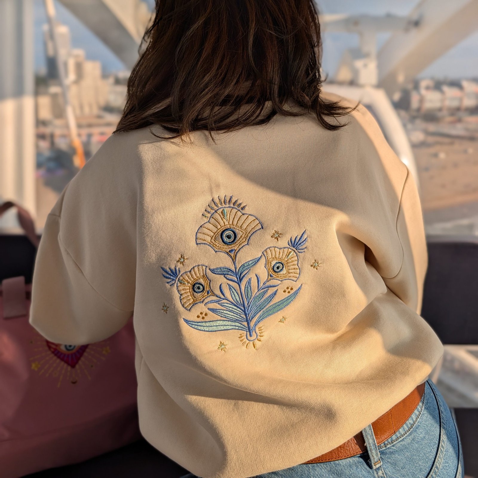 Alexandra, our owner, wearing the Edoaria our mixed cotton embroidered sweatshirt with zipped polo neckline from the Jardin des cyclades collection. Looking in a Ferris Wheel looking the view